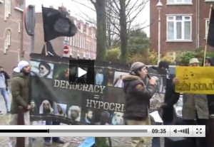 Abou Hafs (rechts) houdt een geel bord op tijdens de toespraak van Oussama C. Links wappert een islamitische vlag, die door ISIS wordt gebruikt.